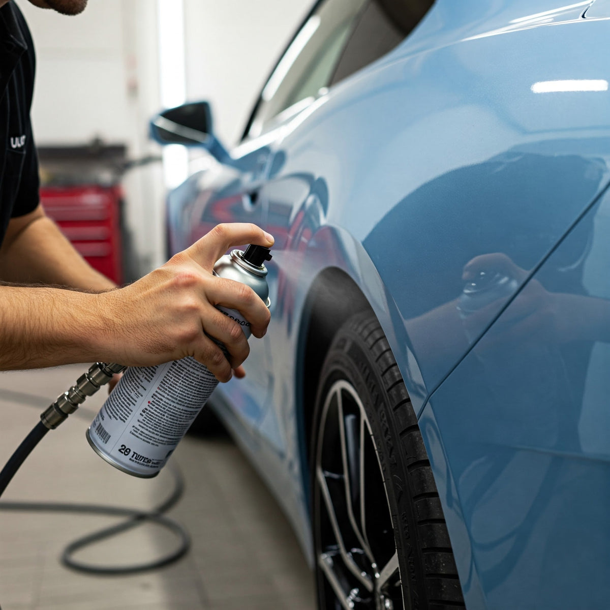 Applicazione di vernice con bomboletta spray sul passaruota di un'auto blu